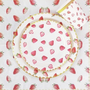 May include: A set of white paper plates and a cup with a gold rim and a strawberry pattern. The plates and cup are decorated with a repeating pattern of red strawberries on a white background.