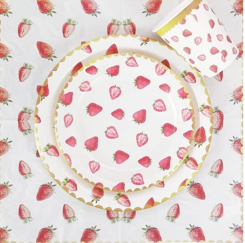 May include: A set of white paper plates and a cup with a gold rim and a strawberry pattern. The plates and cup are decorated with a repeating pattern of red strawberries on a white background.