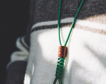 Op de afbeelding: Een groen paracord-koord met een gladde bruine cilindrische kraal en een gevlochten sectie. Het koord bevat een zwart metalen druppelvormig bevestigingspunt verbonden met een zwarte metalen clip, wat zorgt voor een functioneel ontwerp.