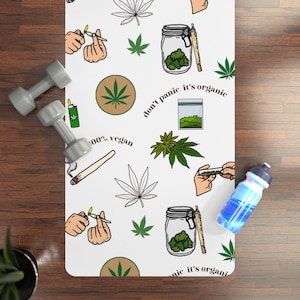 May include: White yoga mat with a repeating pattern of cannabis leaves, joints, jars of buds, and the text "don't panic it's organic" and "100% vegan". Includes a pair of gray dumbbells and a blue water bottle.