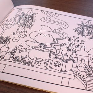 May include: A black and white line drawing of a frog wearing a witch's hat and stirring a cauldron. The frog is surrounded by various potion bottles, candles, and other magical items.