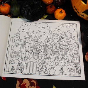 May include: A black and white coloring book page featuring an apple orchard scene. The illustration includes trees with apples, a cat holding a basket, and a character on a ladder. A sign reads "Apple Orchard". Pumpkins and a fence are also visible.