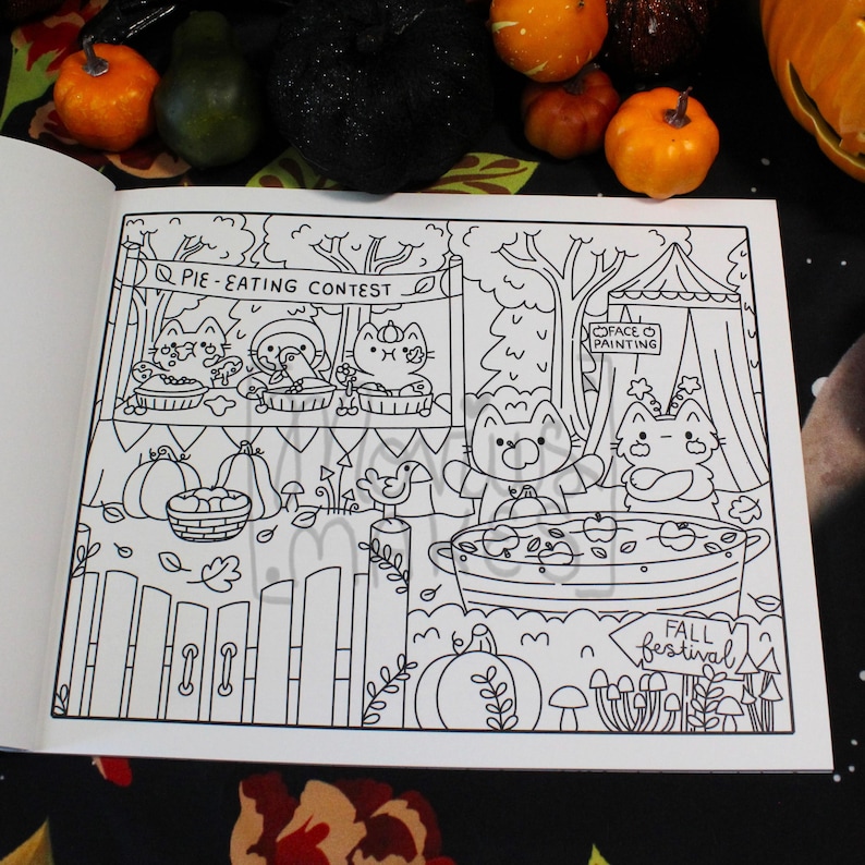 May include: Black and white illustration from a coloring book featuring a fall festival scene. The scene includes a pie-eating contest, face painting, and a large pot with apples. The words "Pie-Eating Contest" and "Fall Festival" are visible.