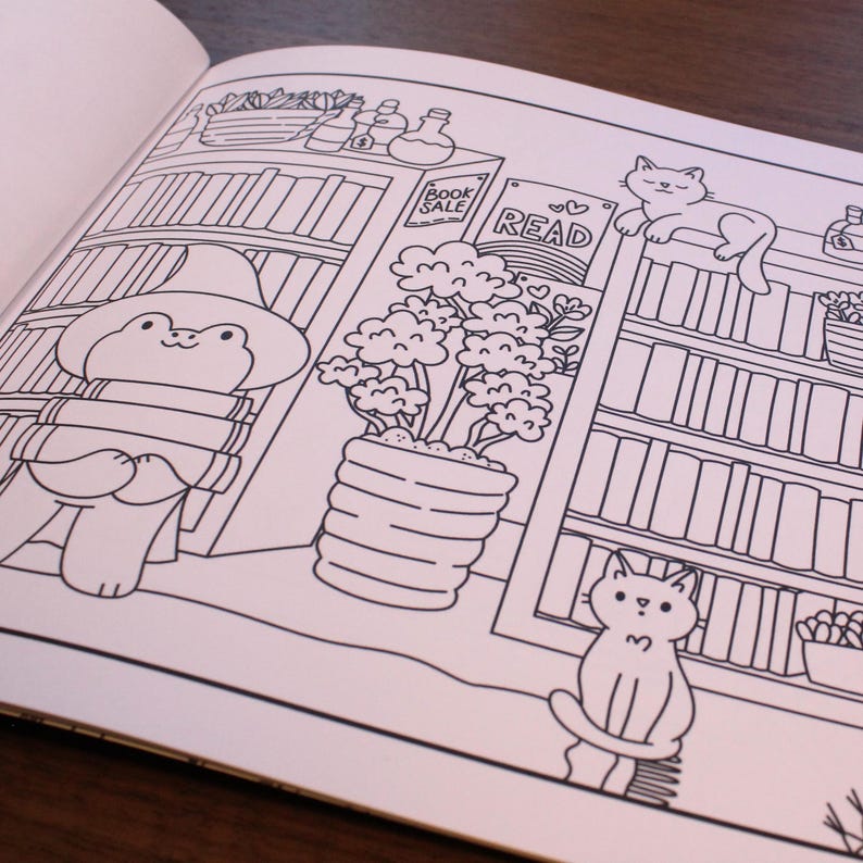 May include: A black and white coloring page featuring a frog wearing a wizard hat and holding books, a potted plant, a bookshelf with books and a sign that says "READ", and two cats.