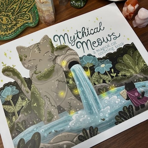 May include: A coloring book titled Mythical Meows: a magical cat coloring book. The cover features a large stone cat statue pouring water from a jar into a stream, with a small black cat in a purple cloak reading a book nearby among flowers.