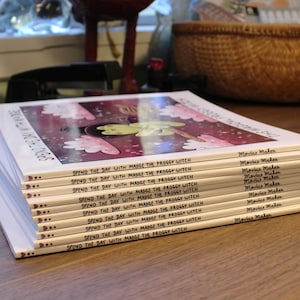 May include: A stack of ten paperback books with a colorful illustration of a frog on a broomstick on the cover. The title of the book is "Spend the Day with Madge the Froggy Witch". The author is Movius Makes.