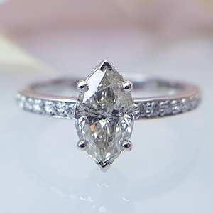 May include: A silver engagement ring with a marquise-shaped diamond set in a pave setting. The ring has a thin band with small diamonds set around the center stone.