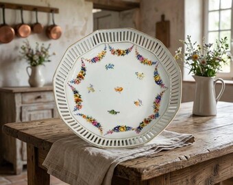 May include: An octagonal serving dish with a white glazed surface featuring polychrome floral swags and individual flower sprigs. The dish has a reticulated lattice rim with a gold trim and measures approximately 12 inches in diameter.