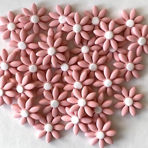 May include: A collection of pink daisy-shaped embellishments with white centers. These decorative flowers are arranged closely together, creating a visually appealing pattern. The petals are a soft pink color.