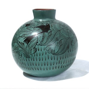 May include: A teal ceramic vase with a black floral and bird design. The vase is round with a small opening at the top.