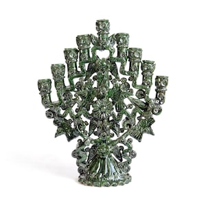 Könnte beinhalten: Ein dunkelgrün glasierter Keramik-Menora-Leuchter mit einem komplizierten, durchbrochenen Design und mehreren Kerzenhaltern in Fächerform. Die Struktur ist mit skulpturalen Vogelfiguren, floralen Motiven und geschwungenen Rankenmustern verziert.