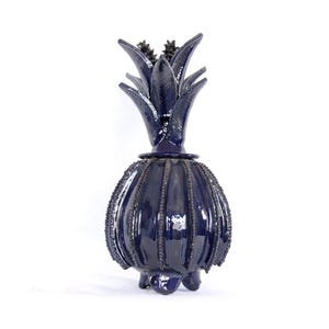 May include: A dark blue ceramic pineapple shaped vase with a textured surface.