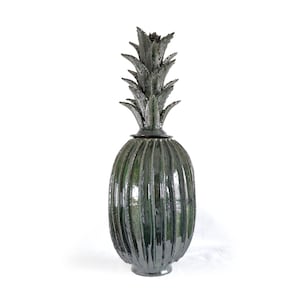 May include: A tall, dark green ceramic pineapple-shaped decorative vase. The vase has a ribbed body and a detailed, textured top resembling pineapple leaves. The base is a solid, rounded shape. The vase is a unique home decor item.