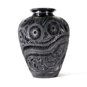 Puede incluir: Un jarrón decorativo negro con intrincados patrones florales y geométricos tallados. El jarrón tiene un cuerpo ancho, un cuello estrecho y una base redondeada. Los intrincados tallados crean una superficie texturizada, agregando profundidad.