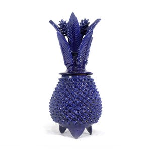 Peut inclure: Un récipient décoratif bleu cobalt en forme d'ananas. Le récipient a un corps texturé et épineux et un dessus feuillu. Il repose sur trois petits pieds. Le design est un objet de décoration intérieure unique et artistique.