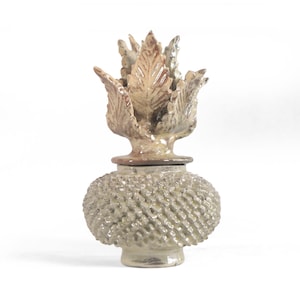 Peut inclure: Pot en céramique décoratif avec un corps texturé et un dessus en forme de feuilles. Le pot est principalement beige clair avec des accents bruns. Le corps bulbeux présente une texture tissée. Idéal pour la décoration intérieure.