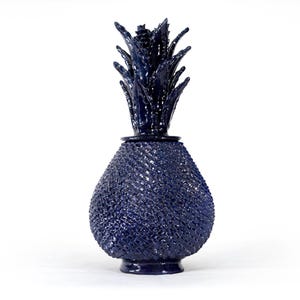 Puede incluir: Un tarro decorativo de cerámica en forma de piña de color azul marino profundo con tapa extraíble. El cuerpo presenta una textura de patrón entrecruzado que imita la piel de la piña, rematado con una corona de hojas esculpidas.