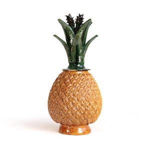 Peut inclure: Un pot en céramique en forme d'ananas avec un corps texturé brun doré et un couvercle amovible orné de feuilles vert foncé brillantes. La base est circulaire et lisse, tandis que le corps présente un motif détaillé en losanges.
