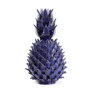 Puede incluir: Escultura de piña de cerámica en un tono índigo oscuro. La piña presenta hojas texturizadas y detalladas y una corona estilizada. La pieza decorativa se encuentra sobre un fondo blanco, resaltando su forma y color.