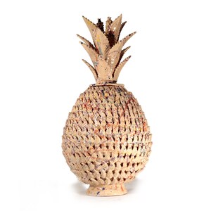 May include: A beige pineapple sculpture with a textured, openwork design. The sculpture has a spiky crown and a small pedestal base. It features accents of red, blue, and yellow. The height is approximately 30 cm.