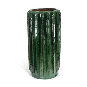 May include: A tall, cylindrical green ceramic vase with a textured, ribbed design. The vase has a glossy finish and a dark brown interior. The vertical ribs are accented with dark brown lines, creating a striking contrast. The vase is a decorative item.