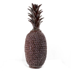 May include: A tall, dark brown pineapple-shaped vase. The body is covered in small, textured details, and the top has a detailed pineapple crown. The vase is approximately 61 cm tall. A decorative item.