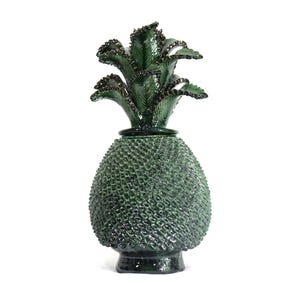 Pode incluir: Um pote de cerâmica em forma de abacaxi verde-escuro com tampa removível. O corpo apresenta uma textura com padrão cruzado, enquanto a tampa é rematada com folhas esculpidas e pontiagudas com bordas castanho-escuras e acabamento brilhante.