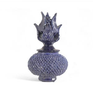 Könnte beinhalten: Eine blaue Keramikvase mit strukturierter Oberfläche und einem stilisierten Blumenverschluss.