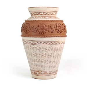 May include: A decorative ceramic vase with a cream-colored base and brown accents. The vase features a floral band and geometric patterns. The vase is approximately 12 inches tall.