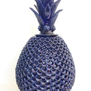 May include: A dark blue ceramic pineapple sculpture with a textured, scale-like body and detailed leaves. The decorative item is handcrafted. The sculpture is a unique piece, ideal for adding a touch of artistry to any space. The measurements are in centimeters.