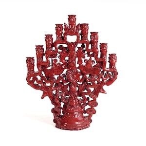 May include: A deep red, ornate candelabra featuring a central vertical structure with multiple branching arms, each topped with a candle holder. The surface is decorated with intricate, raised relief carvings of birds and floral motifs throughout.