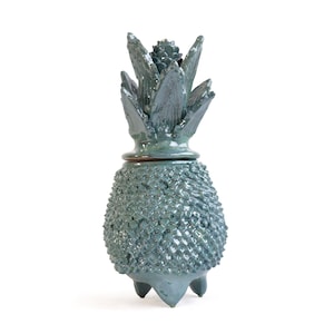 Peut inclure: Un pot en céramique bleu-vert brillant en forme d'ananas. Le corps présente une surface texturée à motifs en losange, tandis que le couvercle amovible est sculpté en forme de feuilles d'ananas pointues et dressées avec un bourgeon central.