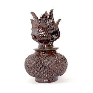 Puede incluir: Objeto decorativo de cerámica marrón oscuro con una base texturizada y bulbosa y una parte superior en forma de flor. El objeto tiene un acabado brillante y está sobre un fondo blanco. El texto "artesanías mexicanas" está en la esquina superior izquierda.