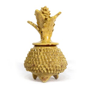 Peut inclure: Un récipient en céramique jaune en forme d'ananas avec un couvercle. Le récipient a un corps texturé et épineux et un dessus feuillu. Il repose sur trois petits pieds, idéal pour la décoration intérieure. Hauteur environ 15 cm.