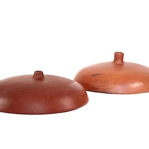 May include: Two terracotta-colored ceramic lids with a small, cylindrical handle on top. The lids are round with a slightly curved surface. One lid is a darker shade of red-brown than the other.