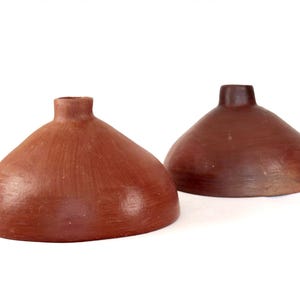 May include: Two terracotta-colored, handmade pottery vases. Each vase has a rounded, bell-like shape with a narrow, cylindrical neck. The vases are displayed against a white background.