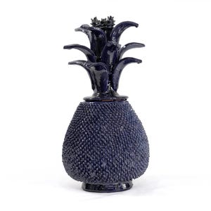 May include: A dark blue decorative pineapple-shaped bottle. The bottle has a textured, dotted surface and a leafy top. The pineapple is a decorative item, likely for display or storage.