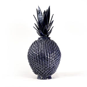 Könnte beinhalten: Eine dunkelblaue dekorative Ananas-Skulptur. Die Ananas hat eine strukturierte, stachelige Außenseite und eine detaillierte, blattartige Oberseite. Die Skulptur besteht aus einem festen Material und steht auf weißem Hintergrund. Die Ananas ist ein einzigartiger Einrichtungsgegenstand.