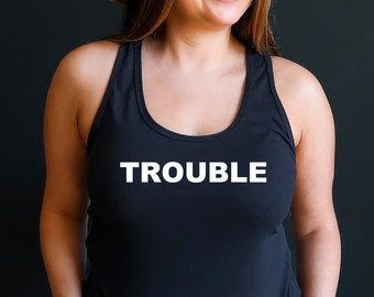 May include: A black tank top with the word "TROUBLE" in white block letters. The person in the image is wearing a tan hat and light blue denim shorts. The background is a solid black.