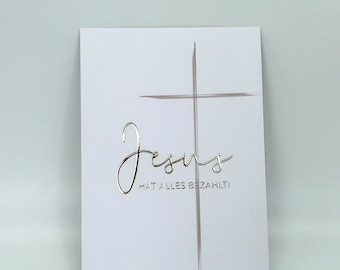 May include: A white card with a silver foil cross and the text "Jesus hat alles bezahlt!" which translates to "Jesus has paid for everything!"