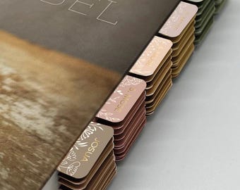 May include: A brown leather-bound Bible with gold lettering on the cover. The Bible has a set of colorful tabs with floral designs and gold lettering, marking different sections of the book.