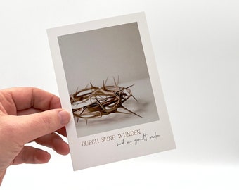 May include: A white card with a brown thorn crown on a white background. The text on the card reads "Durch seine Wunden sind wir geheilt worden."