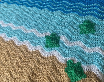 May include: Crocheted blanket with a beach scene featuring blue, white, and tan waves and three green sea turtles.