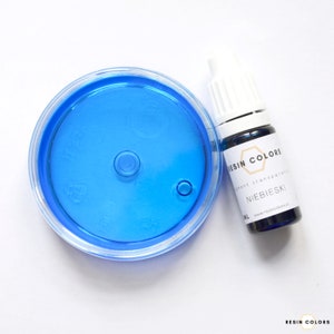 May include: A clear plastic container with a bright blue liquid and a small bottle of blue resin pigment. The bottle has a white cap and a label that reads "RESIN COLORS" and "NIEBIESKI".