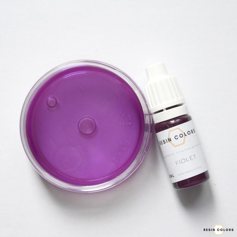 May include: A clear, round container filled with vibrant violet liquid, next to a small bottle labeled "FIOLET" from Resin Colors. The bottle contains a dark purple liquid. The image is on a white background.
