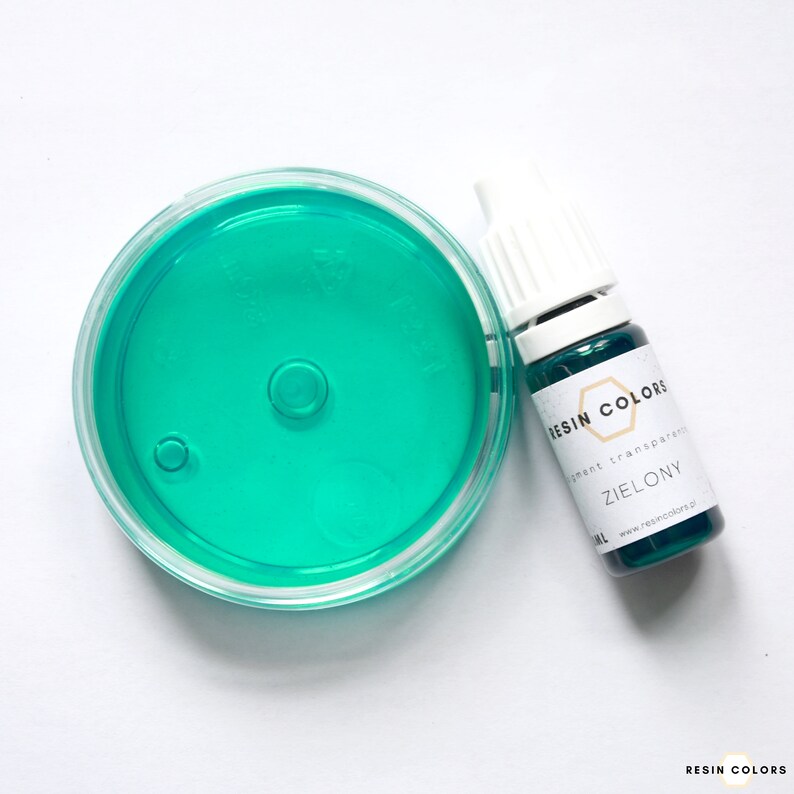 May include: A clear, round container filled with bright teal liquid sits next to a small bottle of green resin pigment. The bottle has a white cap and a label that reads "RESIN COLORS" and "ZIELONY".