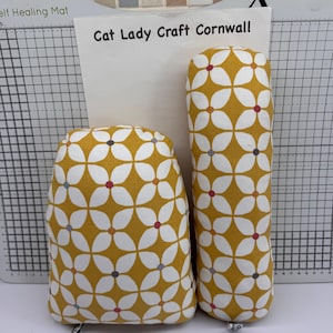 May include: Two fabric items with a floral pattern. The items are mustard yellow with white flower shapes and small red, grey, and blue dots. The text "Cat Lady Craft Cornwall" is visible in the background.