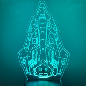 Op de afbeelding: Een turquoiseblauw, lijntekeningontwerp van een ruimteschip, gedrukt op een transparant acryl paneel. Het ruimteschip wordt van achteren verlicht, waardoor een gloeiend effect ontstaat.