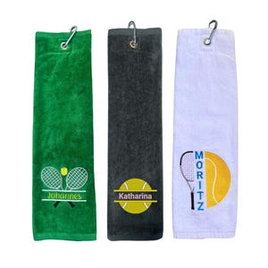 Könnte beinhalten: Drei rechteckige Tennishandtücher in Grün, Grau und Weiß. Jedes Handtuch hat einen silbernen Clip und ein Tennis-Design. Das grüne Handtuch hat den Namen "Johannes", das graue "Katharina" und das weiße "Moritz".