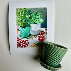 May include: A watercolor painting of two green potted plants on a red and white floral tablecloth. The plants are in green pots with a white pot in the background.